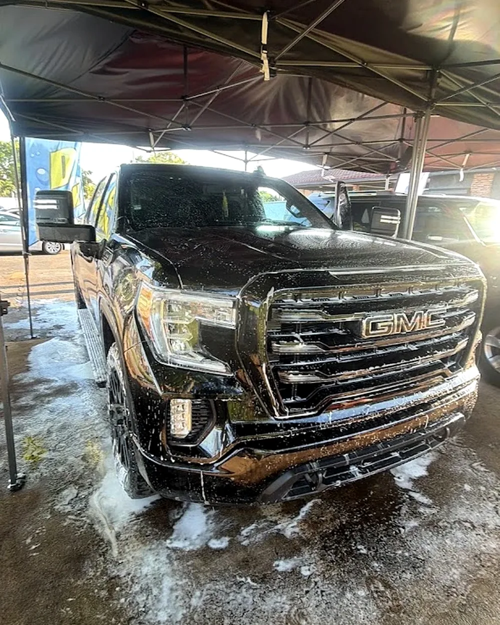 Black GMC Sierra pickup truck undergoing active foam wash under Michael's Detailing canopy